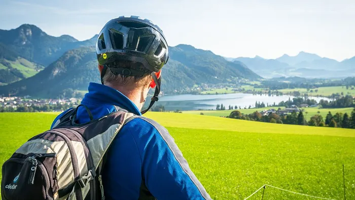 Cyclist with backpack overlooking scenic alpine valley with lake and mountains